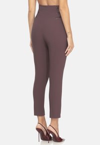 Pantaloni aderenti a vita alta in tessuto bordeaux profondo con una superficie liscia e dettagli laterali, abbinati a scarpe col tacco alto maroon lucido.