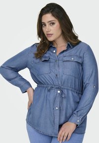 Jeans srajca z svetlo modrim pranjem, dolgi rokavi, gumbasta sprednja zapiranja, dve žepni torbici na prsih in prilagodljiv pas na vrvico. Gladka tekstura.