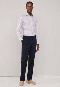 Camicia slim-fit a quadri in rosa chiaro e bianco, abbinata a chinos blu navy e scarpe slip-on beige. Tessuto di cotone morbido, maniche lunghe.