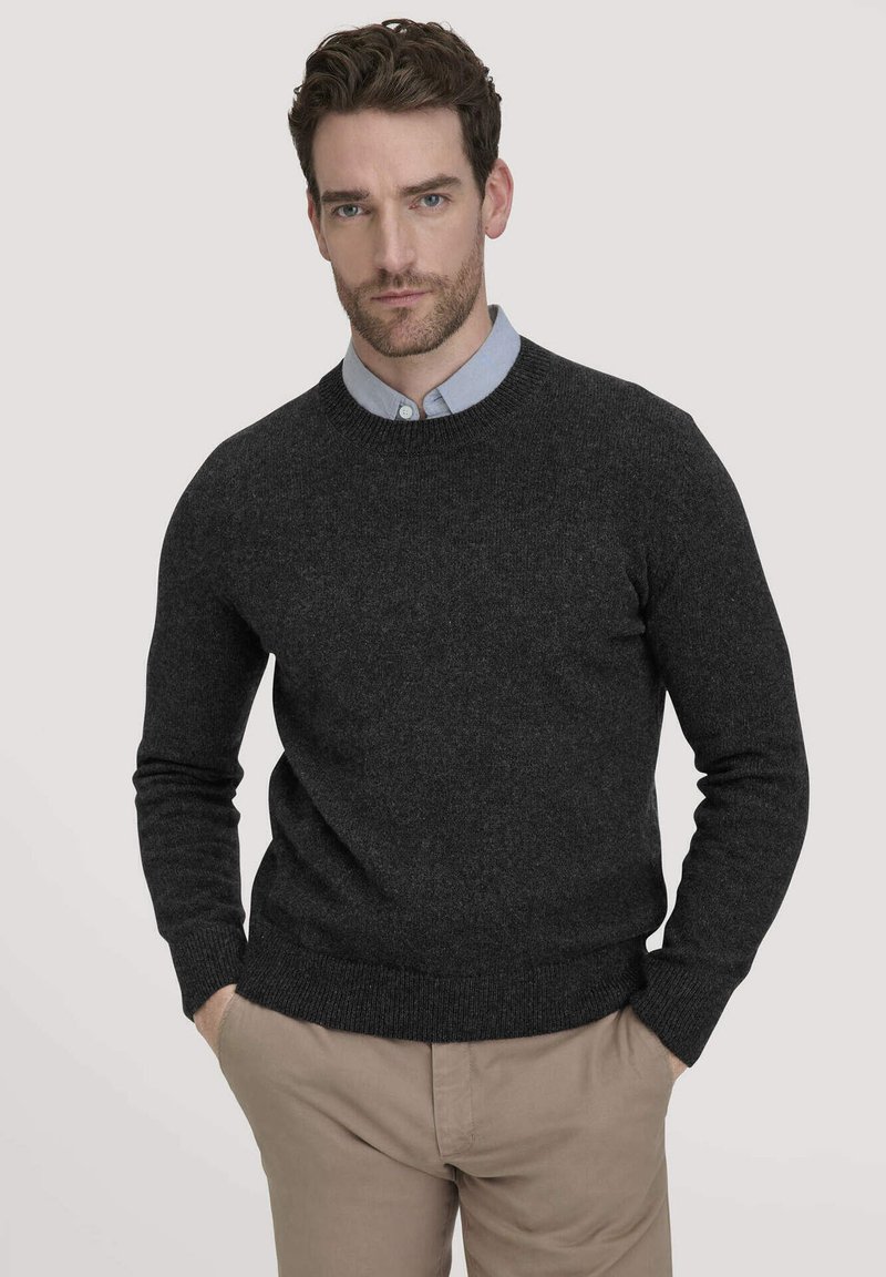 Dunkelgrauer Wollpullover mit Rundhalsausschnitt und gerippten Bündchen, über einem hellblauen Hemd mit Kragen getragen, kombiniert mit beigen Hosen.