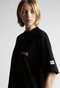 Čierne bavlnené tričko s krátkymi rukávmi, s červenou a bielou grafikou "Wasted" na prednej strane a malou nášivkou na rukáve.