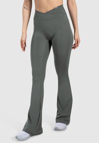 Leggings fitness verde a vita alta con fondo svasato, realizzati in tessuto liscio ed elastico. Presentano un design incrociato in vita.