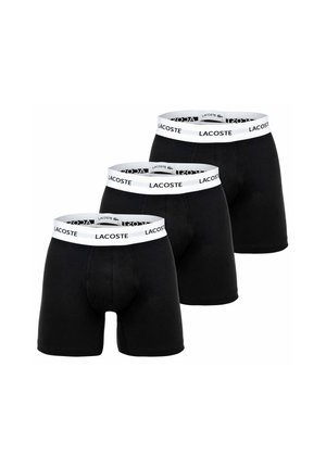 Drie zwarte boxershorts met witte taillebanden waarop de merknaam Lacoste in zwarte letters staat.
