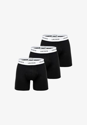 Drei Paare schwarze Boxershorts mit weißen Bundbändern, die den Markennamen Lacoste in schwarzen Buchstaben tragen.