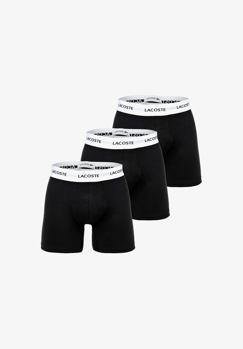 Trois paires de boxers noirs avec des ceintures blanches portant le nom de la marque Lacoste en lettres noires.