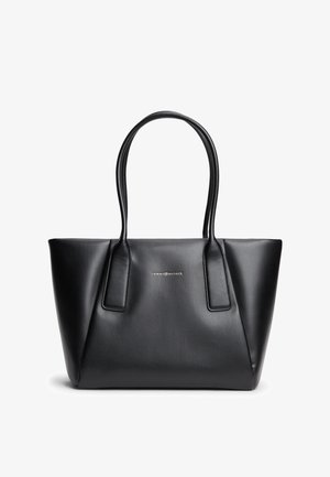 Bolso tote de cuero negro de Tommy Hilfiger con dos asas largas y una forma estructurada trapezoidal sobre un fondo blanco.