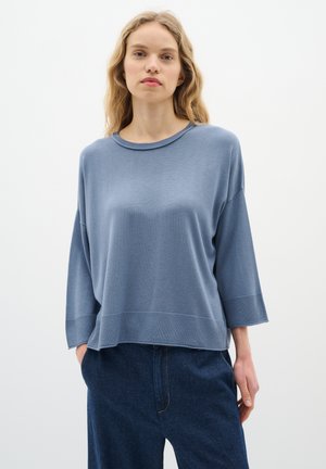 Light blue oversized sweater with a round neckline and three-quarter sleeves, featuring a textured ribbed hem and soft knit material.