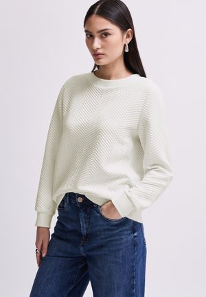 Felpa verde chiaro con un motivo a spina di pesce testurizzato, colletto rotondo e polsini a costine, abbinata a jeans in denim scuro.