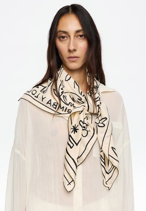 Bufanda de seda en beige con ilustraciones abstractas en negro y texto, atada al cuello. Ligera, de textura suave y forma cuadrada.