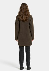 Brun fleecejakke med en afslappet pasform, lange ærmer og længde til midt på låret. Sorte bukser og ankelstøvler fuldender outfittet.