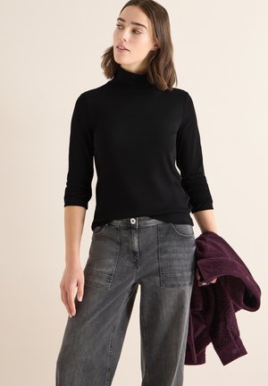 Zwart langemouw turtleneck top, gecombineerd met grijze wijde jeans met pockets en een knoopsluiting. Houdt een gestructureerde paarse jas vast.