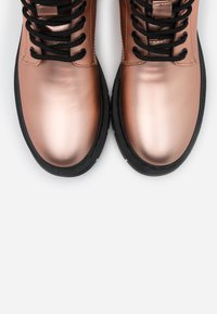 Metalliska roséguld stövlar med svarta snören och gummisulor. Tåområdet är slätt och glänsande, vilket kontrasterar med den strukturerade svarta delen.