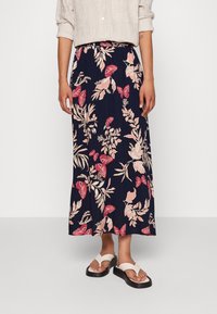 Navy blauwe maxi rok met een bloemen- en vlinderprint in roze en crème, voorzien van een elastische tailleband voor comfort. Draag met witte sandalen.