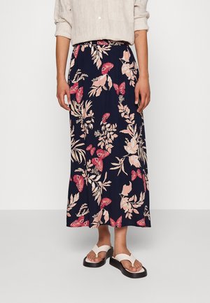 Navy blue maxi skirt with floral and butterfly print in pink and cream, featuring an elastic waistband for comfort. Worn with white sandals.