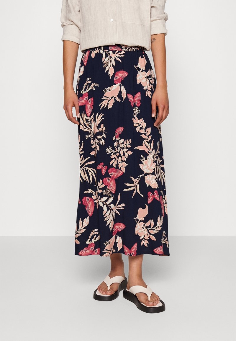 Navy blauwe maxi rok met een bloemen- en vlinderprint in roze en crème, voorzien van een elastische tailleband voor comfort. Draag met witte sandalen.