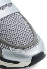 Zapatilla deportiva gris con parte superior de malla, acentos de cuero plateado, collar acolchado y suela de goma negra con detalles texturizados.