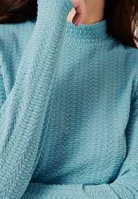 Strickpullover in hellblau mit hohem Rippkragen, ausgestattet mit einem Zickzackmuster und langen Ärmeln. Der Stoff wirkt weich und gemütlich.