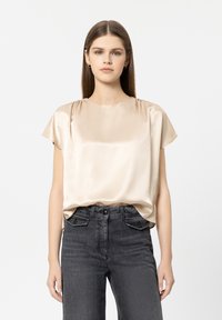 Satin-Kurzarm-Top in sanftem Beige, Rundhalsausschnitt, lockere Passform, kombiniert mit dunkelgrauen, hoch taillierten Jeans. Minimalistisches Design.