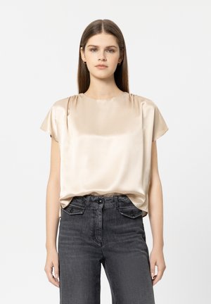 Satin-Kurzarm-Top in sanftem Beige, Rundhalsausschnitt, lockere Passform, kombiniert mit dunkelgrauen, hoch taillierten Jeans. Minimalistisches Design.