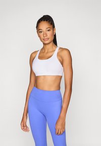 Nike sportbeha in het wit met een ronde halslijn en brede bandjes, gecombineerd met hoog getailleerde blauwe leggings met een gladde textuur.