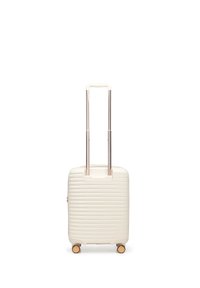 Walizka z twardą skorupą w kolorze kremowym o pionowej żebrowanej fakturze, z dwoma kółkami w odcieniu złota i wysuwanym srebrnym uchwytem.