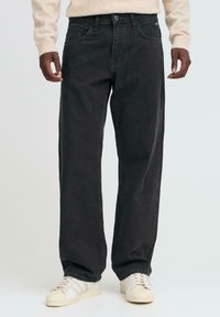 Jeans negri din denim cu croială dreaptă, având cinci buzunare, bucle pentru curea și cusături contrastante, asortați cu adidași albi.