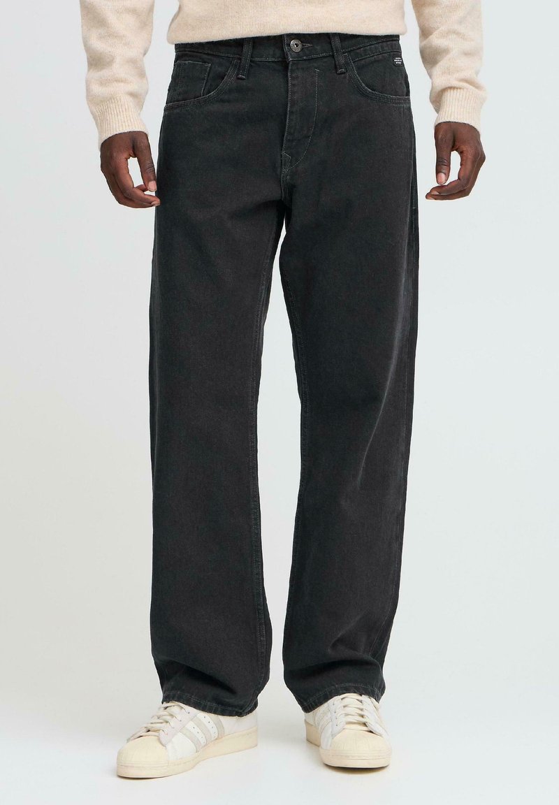 Jeans negri din denim cu croială dreaptă, având cinci buzunare, bucle pentru curea și cusături contrastante, asortați cu adidași albi.