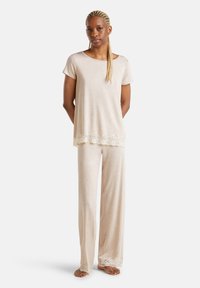 Crème-kleurige pyjama set met een top met korte mouwen en kantafwerking en losse broeken met bijpassend kant aan de zoom. Zachte stoftextuur.