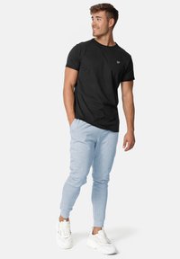Schwarzes Baumwoll-T-Shirt, Rundhalsausschnitt, kurze Ärmel, kombiniert mit hellgrauen Jogginghosen, an den Bündchen eng anliegend, getragen mit weißen Sportschuhen.