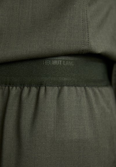 Tecido verde oliva com uma textura suave, apresentando uma cintura franzida. Nome da marca em relevo "HELMUT LANG" visível na faixa.
