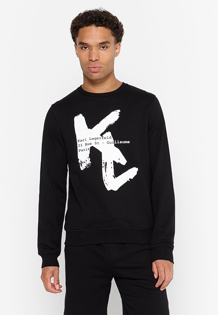 Sudadera negra hecha de una tela suave, con un gran logotipo de pincelada blanca y texto en una fuente moderna en el pecho. Cuello y puños acanalados.
