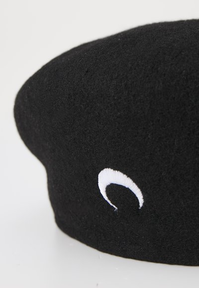 Boina de lana negra con una textura suave, que presenta un acento bordado en blanco. El diseño es redondo y ligeramente elevado en la parte superior.