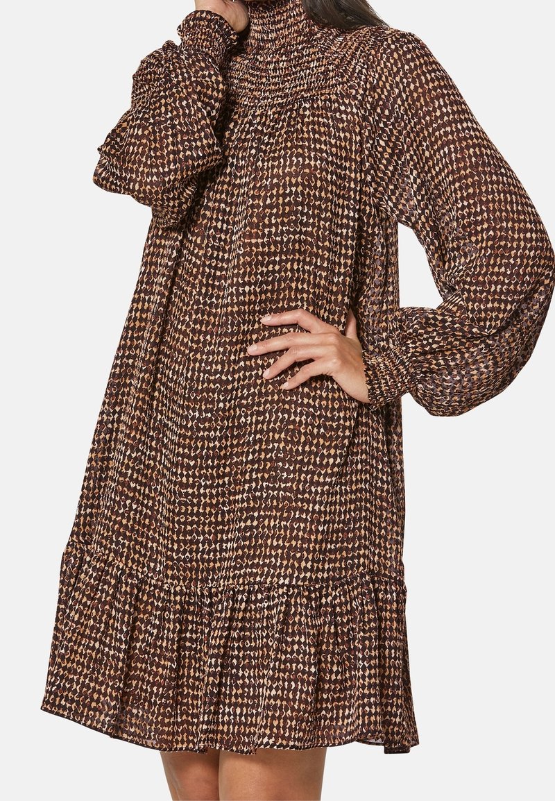 Braun gemustertes Kleid mit langen Ärmeln, hohem Kragen und fransigem Saum. Hergestellt aus strukturiertem Stoff mit einer Mischung aus hellen und dunklen Farbtönen.