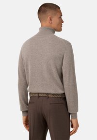 Pull gris clair avec un col montant, texture tricotée et manches longues, associé à un pantalon marron et une ceinture tressée.