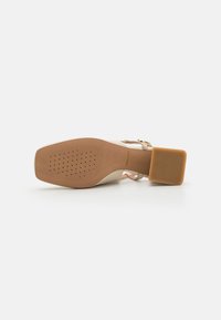 Beige høyhælte sko med firkantet hæl, teksturert såle og justerbar rem. Glatt skinnfinish med perforeringer for pusteevne.
