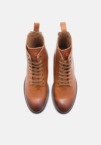 Botas de cuero marrón hasta el tobillo con un acabado suave, punta redondeada y cierre con cordones. Presentan un tirador en la parte trasera y un detalle de marca sutil.