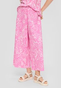 Roze culottebroeken met een wit bloemenpatroon en een gestructureerde stof. Gecombineerd met lichtbeige sandaal met gevlochten accenten en dikke zolen.