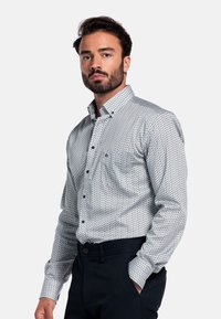 Overhemd met knoopsluiting in een blauw-wit geometrisch patroon, gemaakt van lichtgewicht stof. Beschikt over een klassieke kraag en een enkele borstzak.