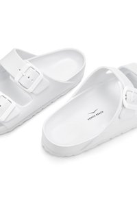 White slip-on sandals with two adjustable straps featuring buckles, textured sole, and embossed "VENICE BEACH" logo inside.