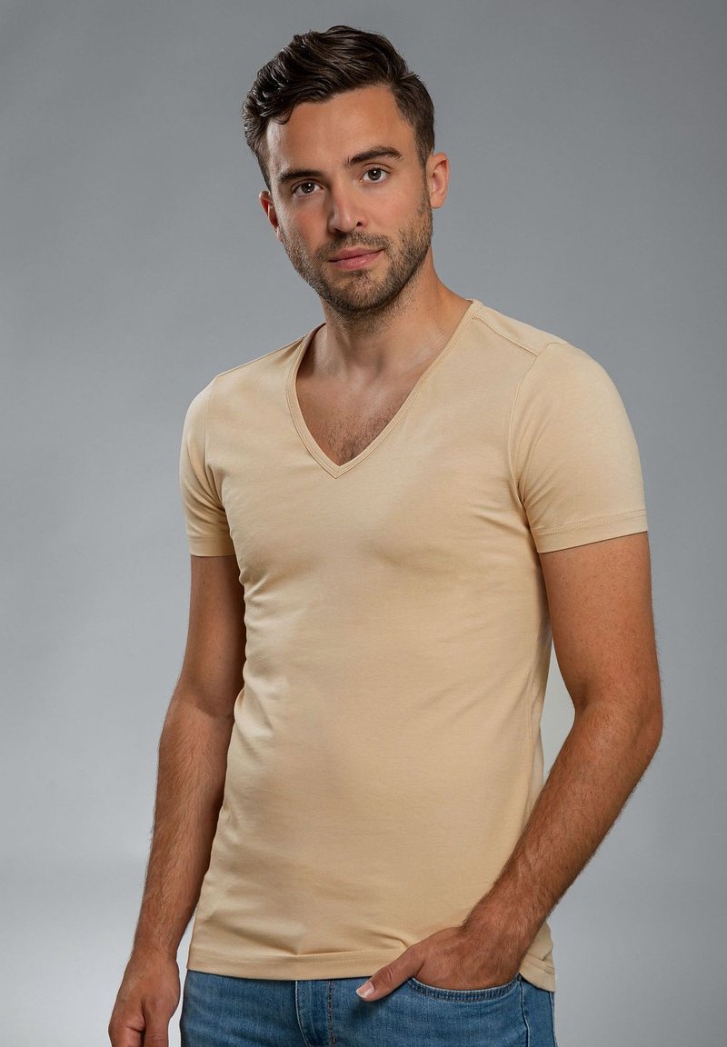 Beige V-hals T-shirt, korte mouwen, aansluitend ontwerp, soepele textuur, gemaakt van een katoenmix, gecombineerd met lichtblauwe jeans.