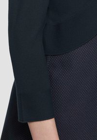 Maglione navy a maniche tre quarti con polsini a coste, abbinato a una gonna scura a pois con piccole macchie bianche.