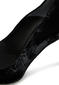 Scarpa con tacco alto in velluto nero, decorata con un ornato motivo floreale, caratterizzata da un design curvo elegante e una superficie texturizzata.