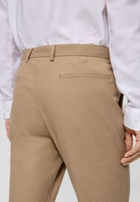 Tan dress pants with a smooth texture, tailored fit, and two back pockets; paired with a light-colored shirt.