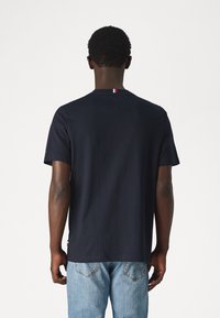 Camiseta corta de manga en navy con cuello redondo, que presenta una pequeña franja roja, blanca y azul en la parte posterior, y jeans de color azul denim.