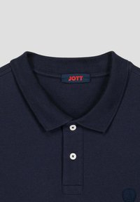 Marineblauwe polo met een gestructureerde stof, drie witte knopen en een klein geborduurd logo op de linkerkant van de borst. Rood "JOTT" label op de kraag.