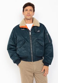 Marineblauwe gewatteerde bomberjack met een nepleren kraag, oranje binnenvoering, ritssluiting en voorzakken. Beschikt over een zijzak en een logo patch.