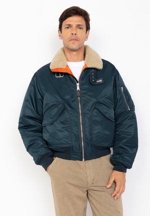 Marineblauwe gewatteerde bomberjack met een nepleren kraag, oranje binnenvoering, ritssluiting en voorzakken. Beschikt over een zijzak en een logo patch.