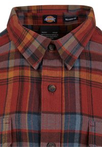 Red and orange plaid flannel shirt with a collared neck, button closure, and two chest pockets. Features a relaxed fit and textured fabric.