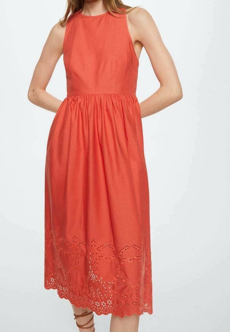 Robe midi corail sans manches avec taille froncée et ourlet à découpe florale œillet portée par une personne les mains dans le dos.