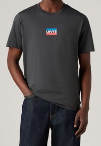 Šedé bavlněné tričko s krátkým rukávem a kulatým výstřihem má na hrudi vícebarevnou nášivku s logem Levi's. Kombinováno s tmavými džíny.